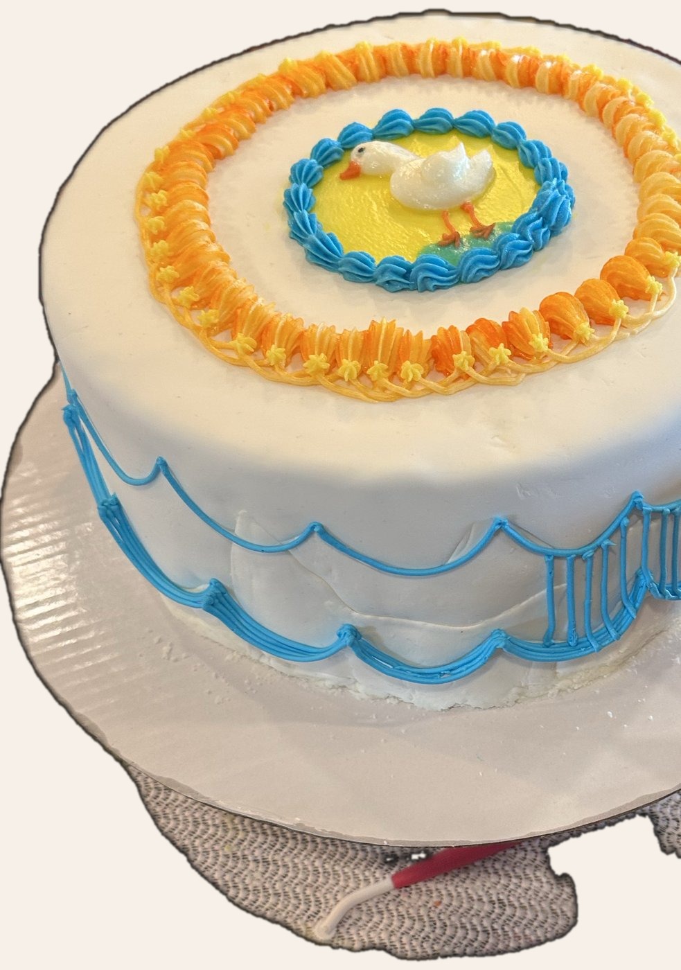 White cake with yellow duck medallion, blue wave piping, and orange star border