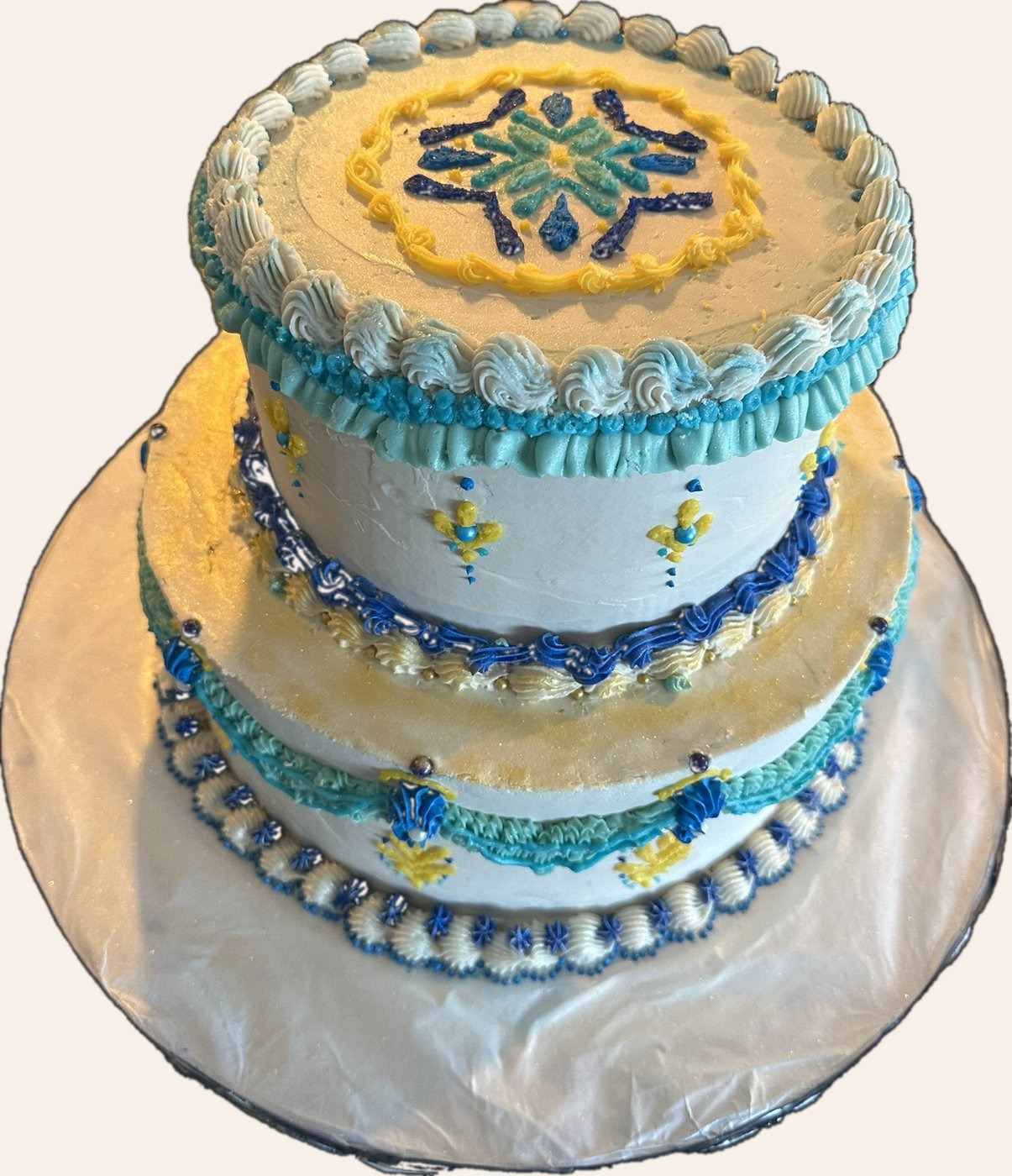 Two-tier white cake decorated with blue and yellow snowflake motifs