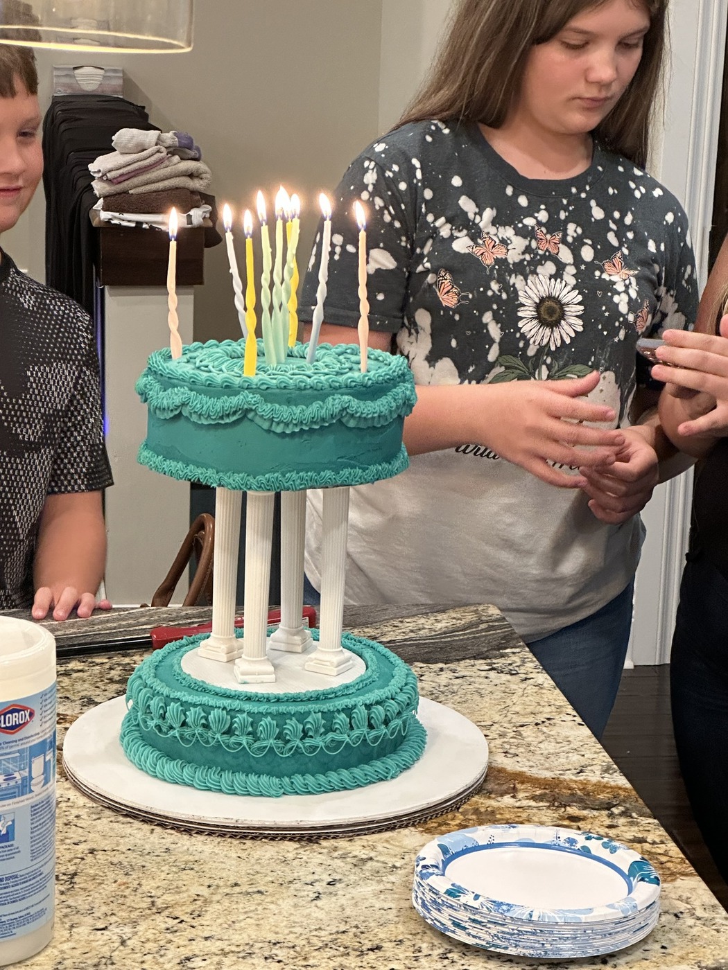 Two-tier teal cake with ornate piping, white pillars, and lit spiral candles